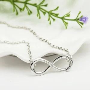 Silver plated infinity necklace on white background with greenery